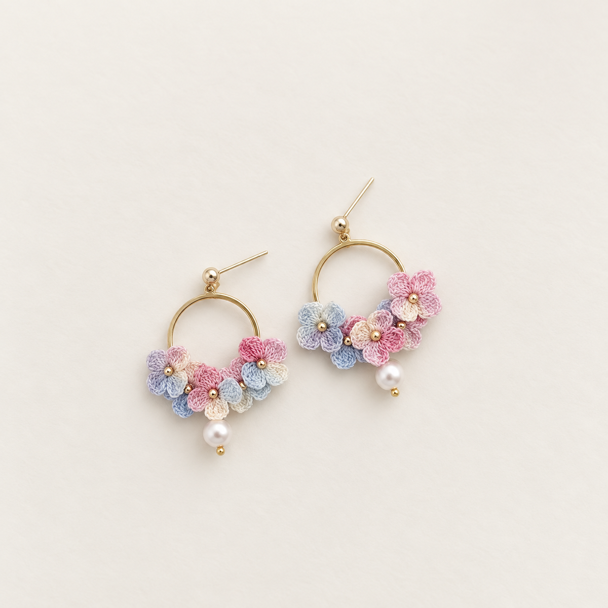 Pastel rainbow micro crochet hydrangea hoop earrings with pearl drops, pair on ivory background