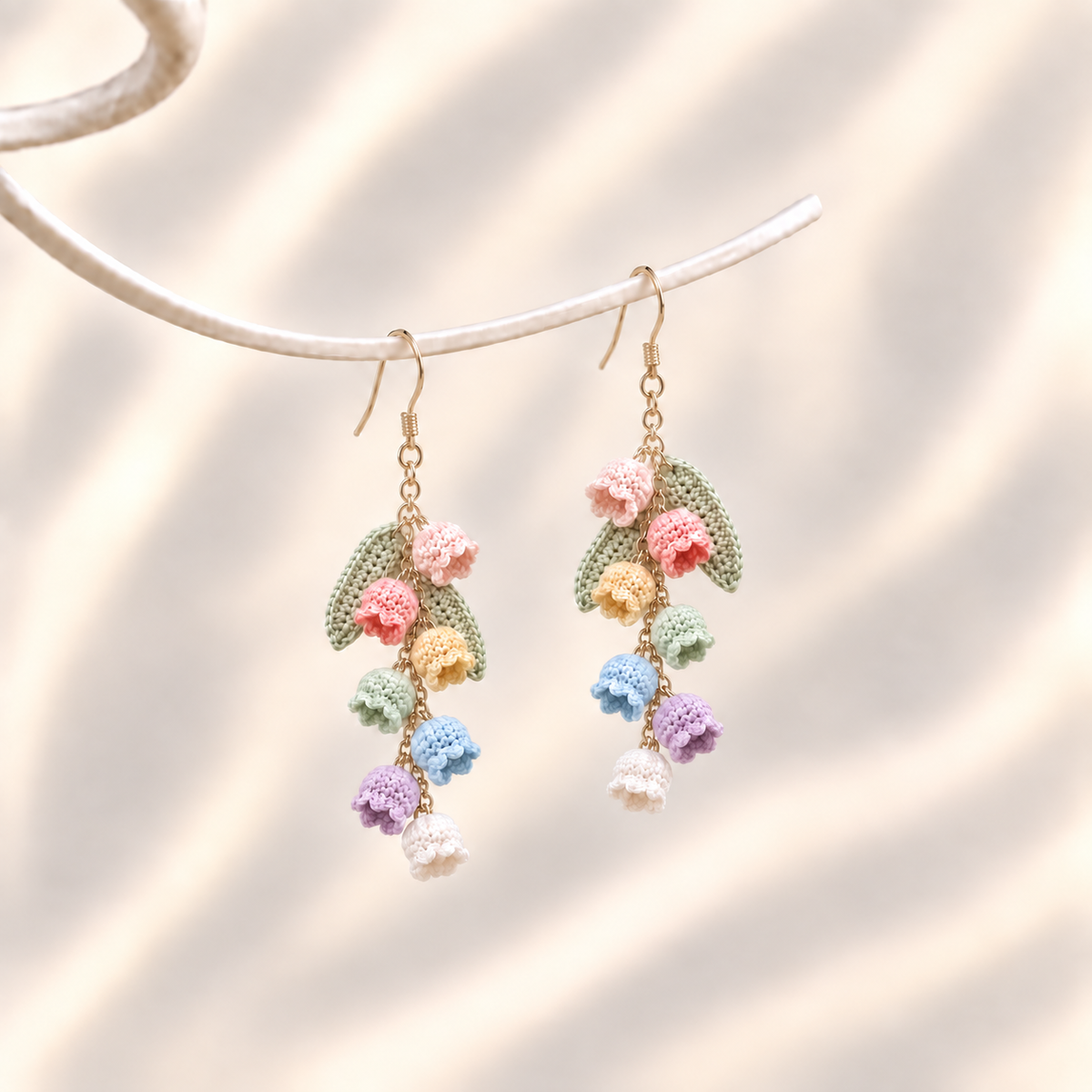 Petalore rainbow bell flower micro crochet earrings — pair on an ivory display